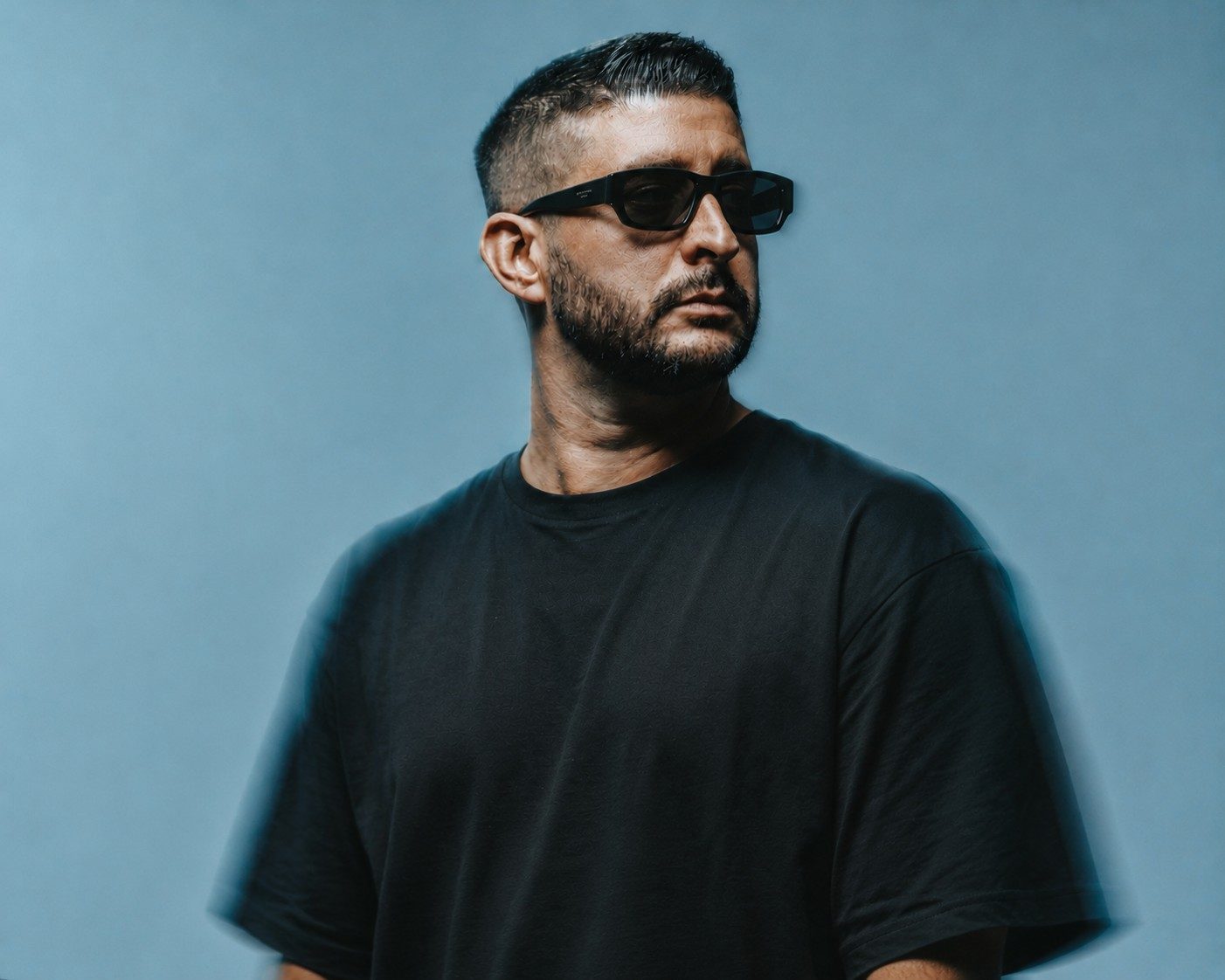Martin OCCO in a black t-shirt and sunglasses against a blue-grey backdrop